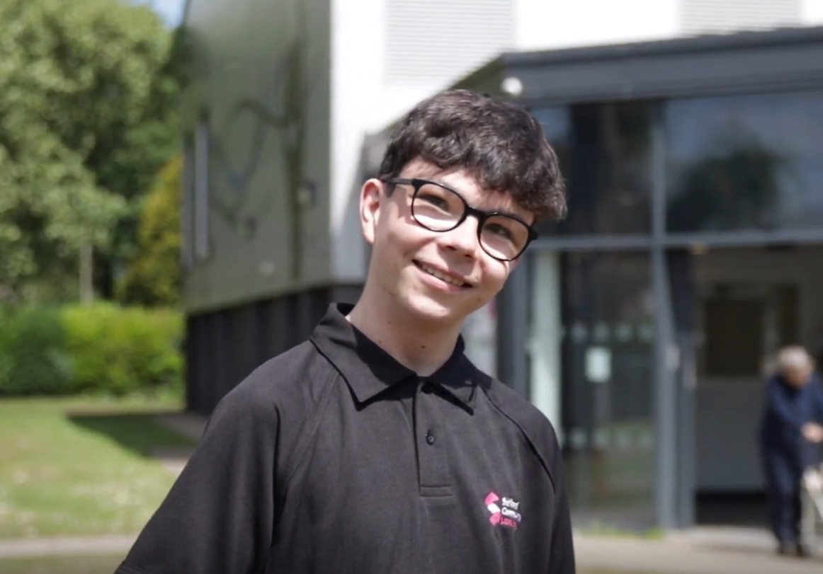 A smiling young man stood in front of a grey and black building