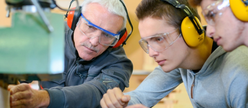 A man in a workshop showing two young men how to use some machinery
