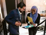 A man and a woman stood on the stairs in an office looking at a report