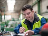 A young man with learning difficulties in a high visibility jacket in a work place