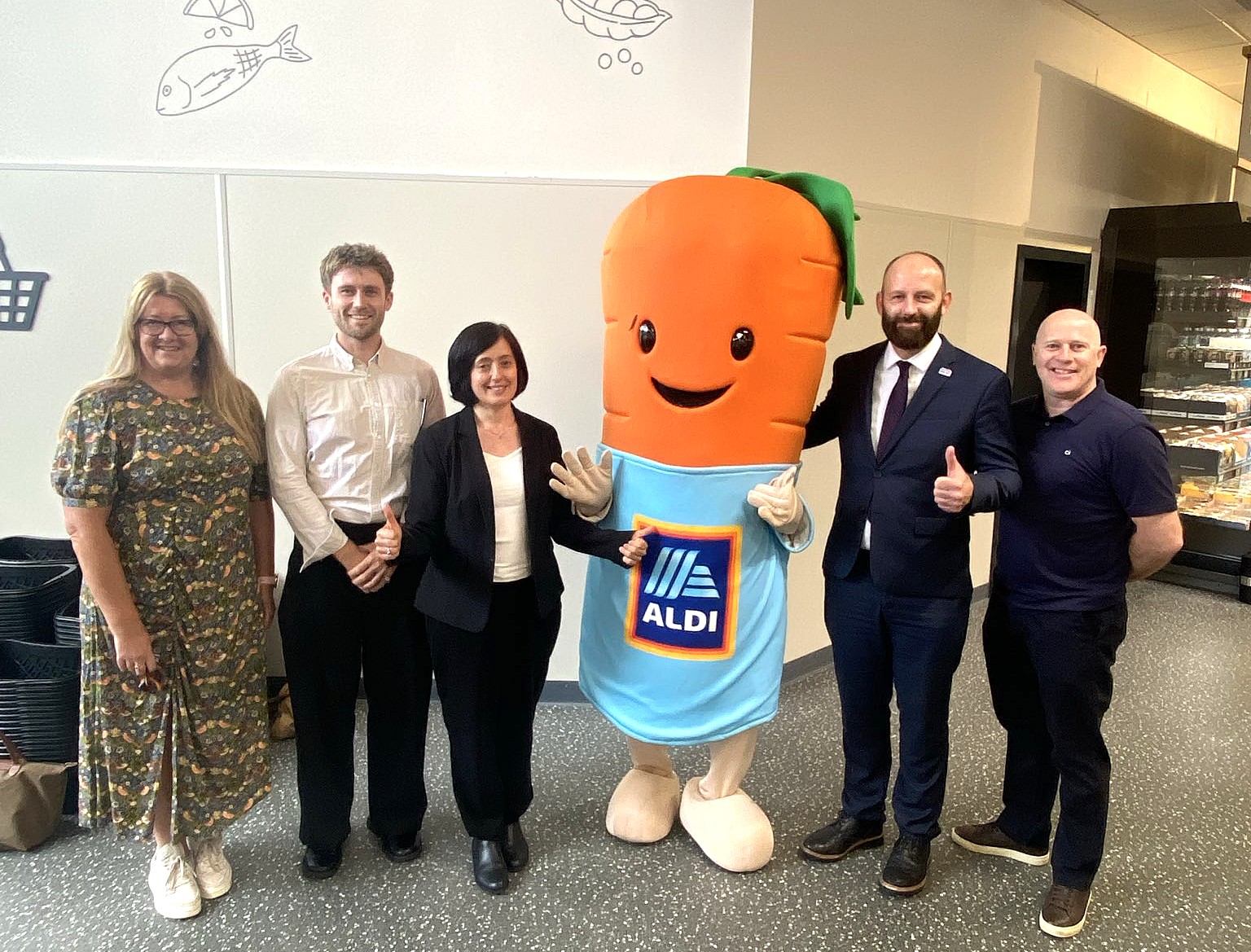 Five people stood smiling with Kevin the Carrot in a supermarket